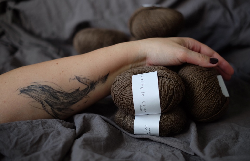 Рука с татуировкой, держащая мотки пряжи Knitting for Olive Merino | Arm with tattoo holding skeins of Knitting for Olive Merino yarn