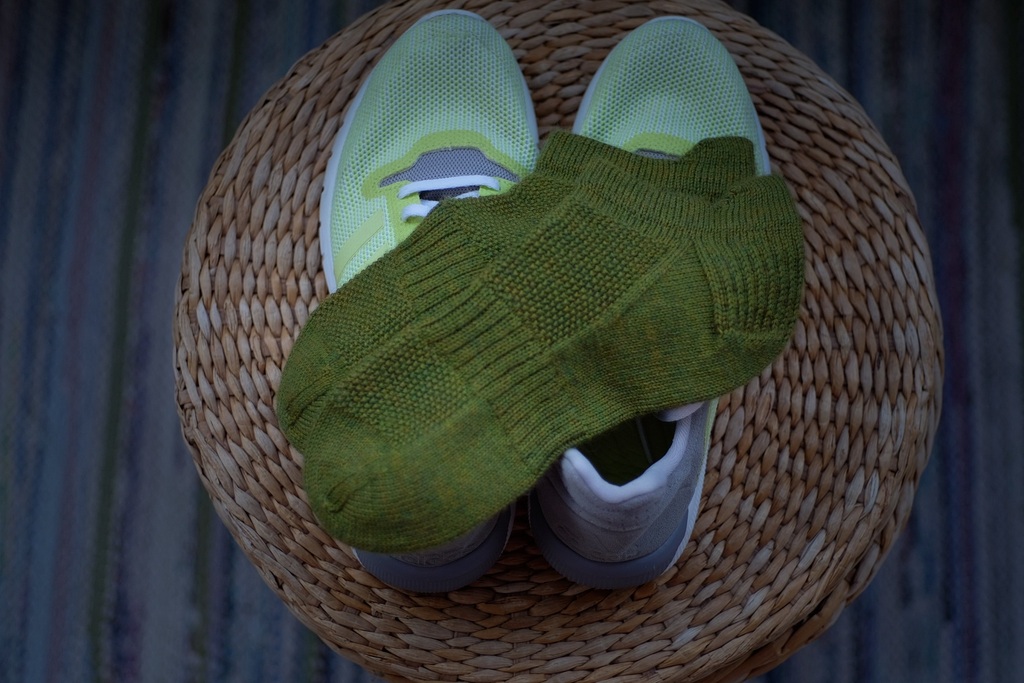 Green So Sporty Socks resting on a pair of yellow running shoes, displayed on a wicker basket.