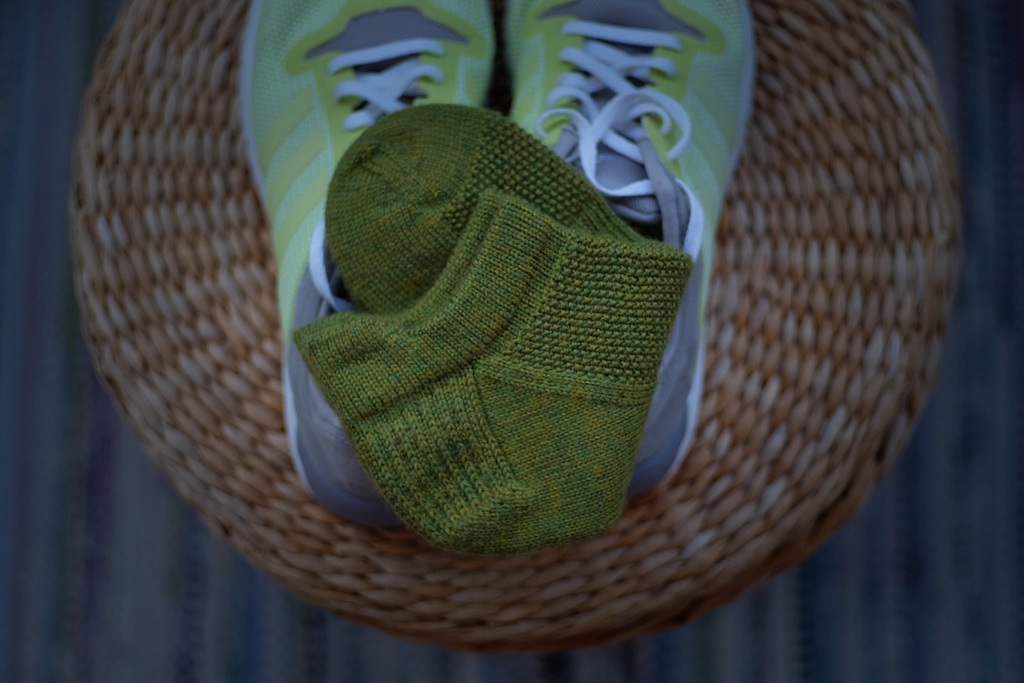 Green So Sporty Socks placed on top of a pair of yellow running shoes, viewed from above.