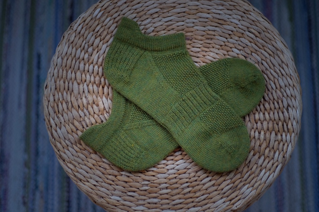 Green So Sporty Socks neatly arranged on a wicker basket, highlighting the detailed knitting pattern.
