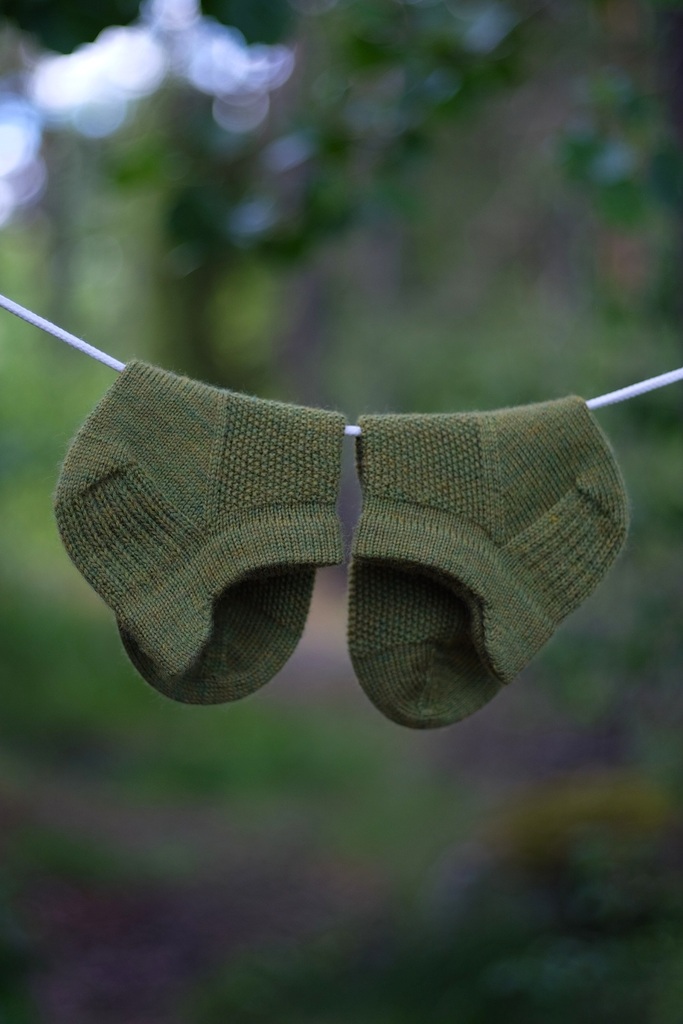 Green So Sporty Socks hanging on a clothesline with a blurred forest background.