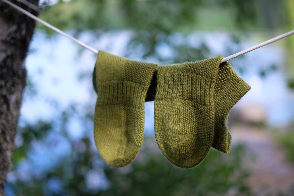 Green So Sporty Socks hanging on a clothesline with a blurred forest background.